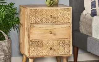 Wooden three-drawer bedside table placed beside bed with plant decor.