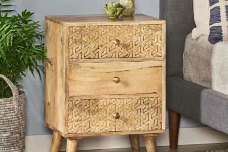 Wooden three-drawer bedside table placed beside bed with plant decor.