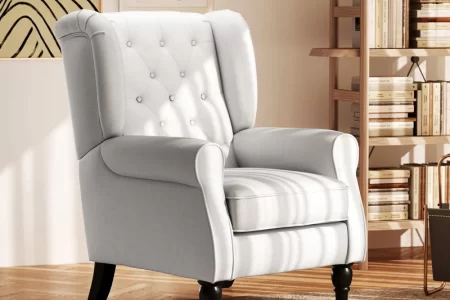 White fabric wingback armchair with tufted backrest in reading area.