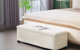 Cream upholstered storage bench at foot of bed with book.
