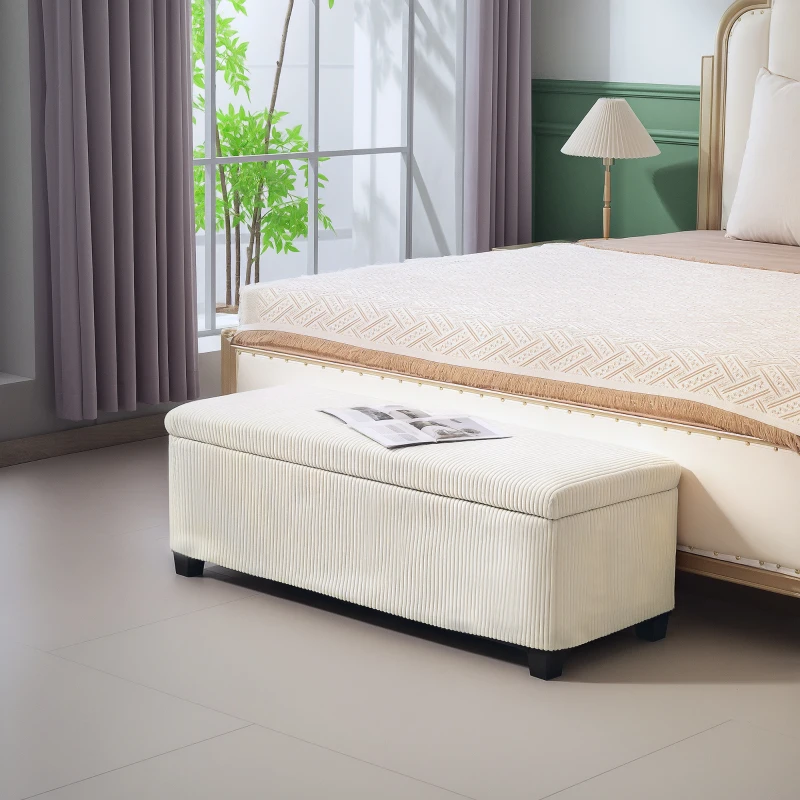 Cream upholstered storage bench at foot of bed with book.
