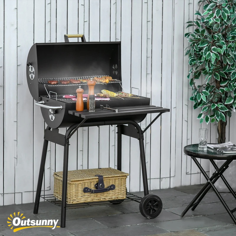 Black charcoal grill with food cooking outdoors beside table.