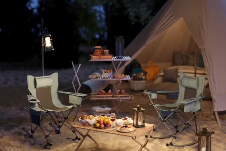 Camping chairs arranged near tent with lanterns and food setup