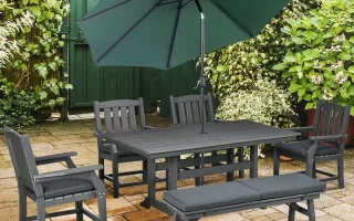 Outdoor patio dining set with green umbrella and cushioned seating on stone patio.