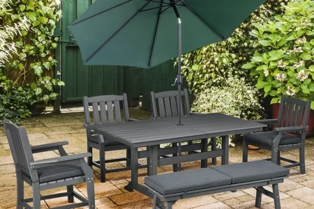 Outdoor patio dining set with green umbrella and cushioned seating on stone patio.