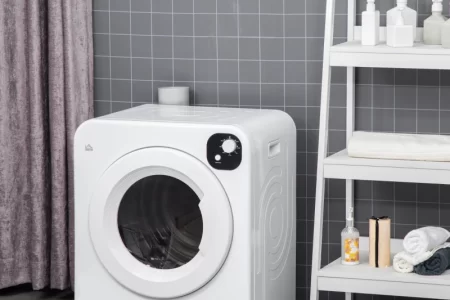 Compact white HOMCOM laundry dryer placed beside shelf in tiled laundry room