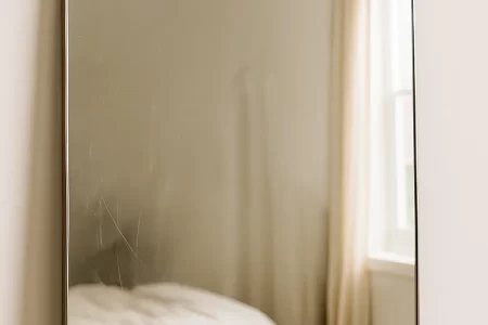 Lightly scratched mirror reflecting a bedroom before the scratch removal process.