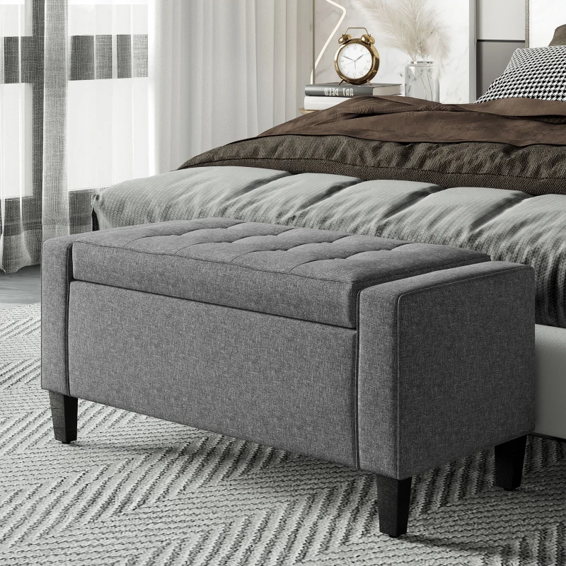 Dark gray upholstered ottoman placed at foot of cozy bed
