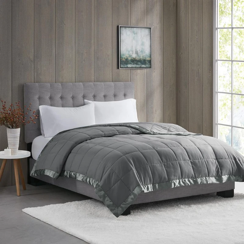 Grey quilted blanket neatly spread on a modern upholstered bed with white pillows.