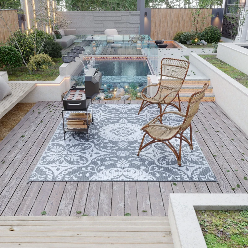 Patio setup with wicker chairs and gray-white floral rug beside pool.