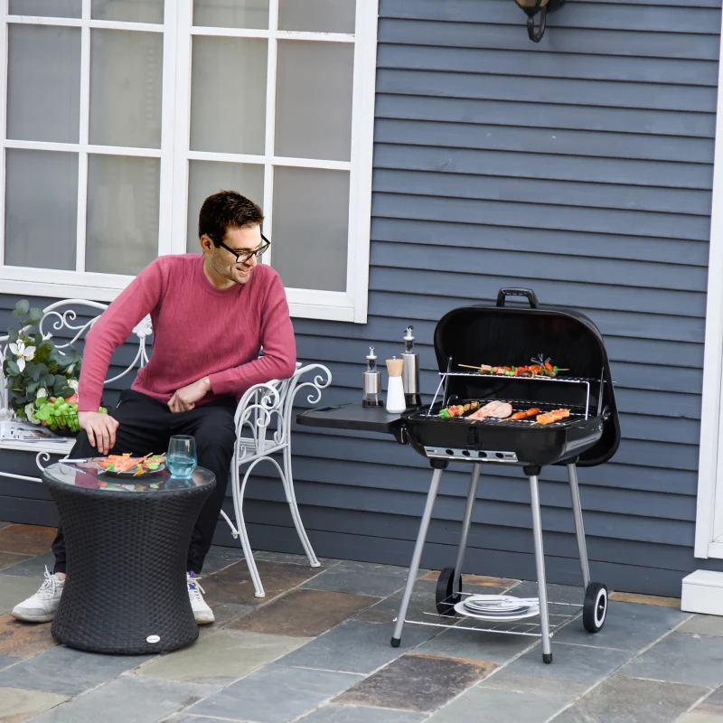 Man sitting near black charcoal grill cooking skewers outdoors.