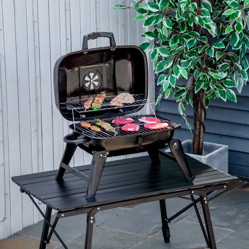 Small tabletop charcoal grill with meats cooking on rack.