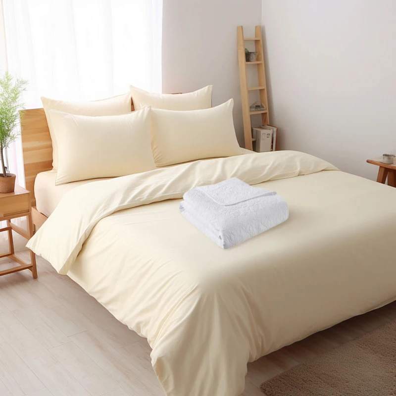 Cream bedding set with folded white quilt placed on top in a cozy bedroom.