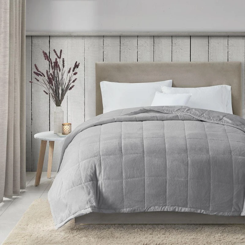 Soft gray quilted blanket neatly spread on a beige bed in a bright bedroom.