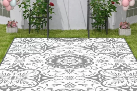 Outdoor setup with white and gray floral rug on grass, surrounded by balloon decorations and garden flowers.