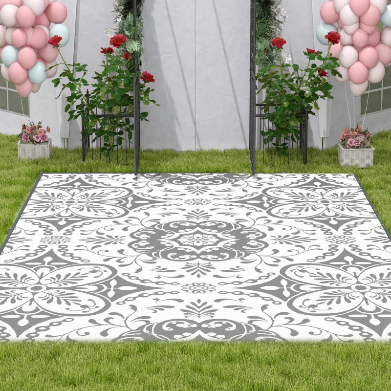 Outdoor setup with white and gray floral rug on grass, surrounded by balloon decorations and garden flowers.