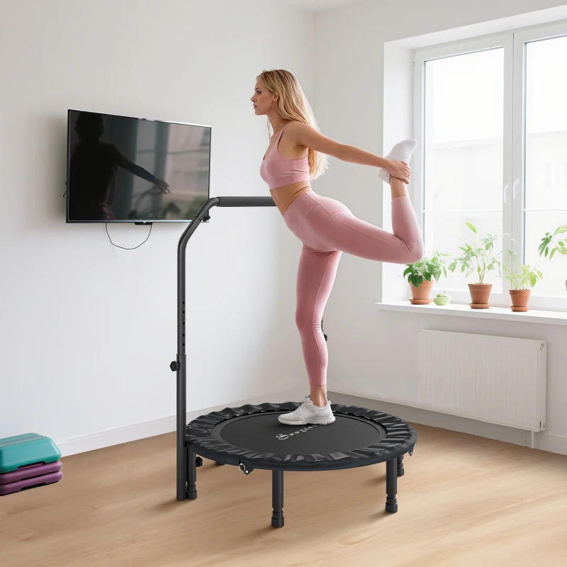 Woman stretching leg on mini trampoline with handlebar in home gym.