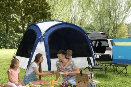 Family enjoying picnic beside blue camping tent and parked SUV
