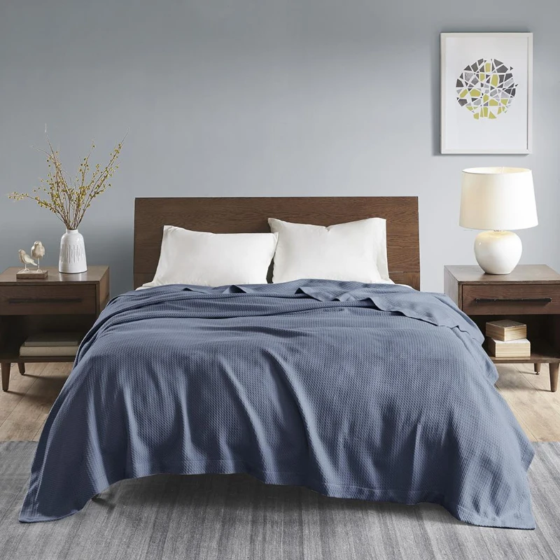 Blue cotton blanket laid across a wooden bed with white pillows and nightstands.