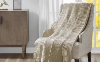 Beige quilted blanket draped over an armchair in a bright living room.