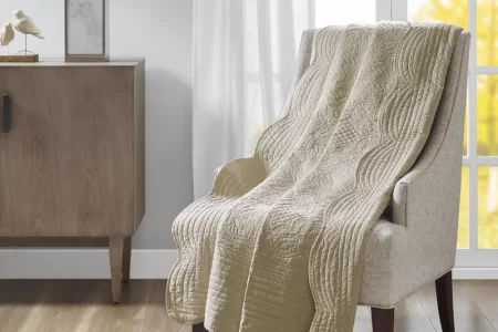 Beige quilted blanket draped over an armchair in a bright living room.