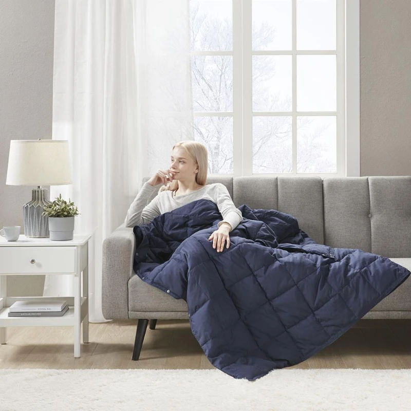 Woman sitting on a gray sofa covered in a navy quilted down throw.