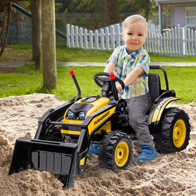 Smiling boy playing on yellow toy bulldozer pushing sand outdoors.