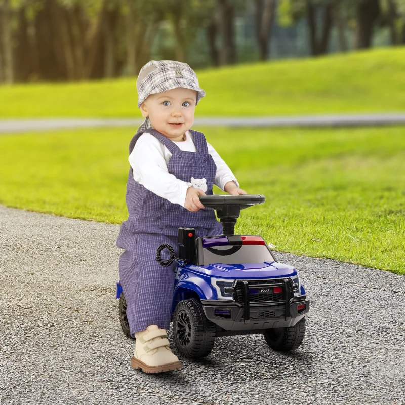 Toddler sitting on blue ride-on police toy truck on park path.

