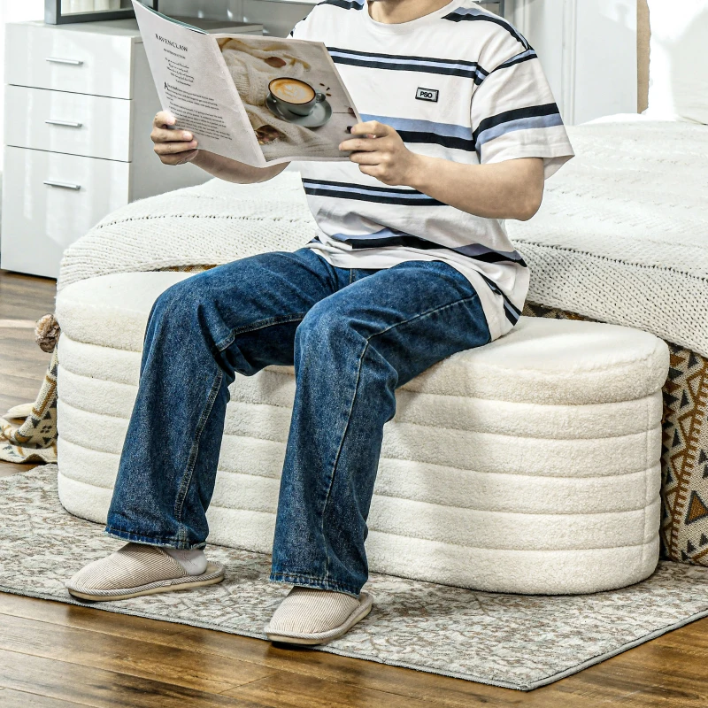 Person reading magazine while seated on cream bedroom bench.