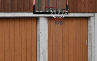 Wall-mounted basketball hoop with glass backboard above garage doors