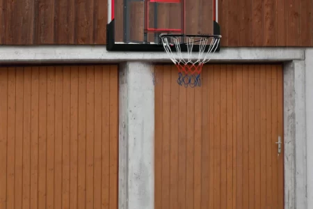 Wall-mounted basketball hoop with glass backboard above garage doors