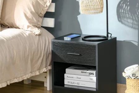 Modern black nightstand beside bed with lamp and books.