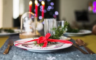 Single plate with rosemary sprig, red ribbon, and copper cutlery on a festive runner.