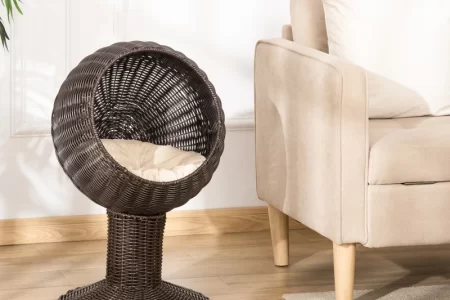 Elevated dark rattan cat bed with cushioned interior placed beside a beige sofa.