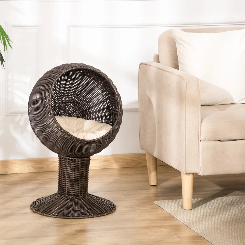 Elevated dark rattan cat bed with cushioned interior placed beside a beige sofa.
