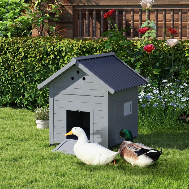 Two ducks standing beside a small grey outdoor duck house.
