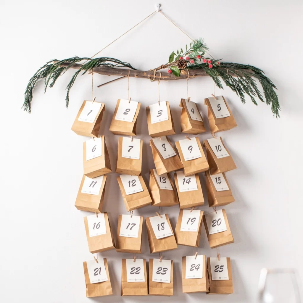Hanging DIY advent calendar with numbered paper bags on a branch.