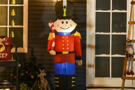 Large inflatable nutcracker holding candy cane outside festive house.