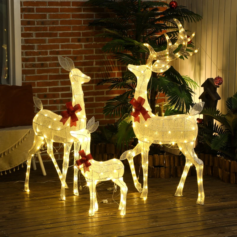 Three illuminated reindeer with red bows on wooden deck at night.