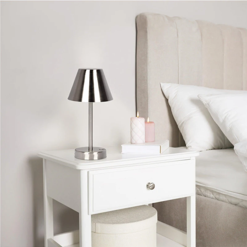 Sleek metal table lamp on white nightstand next to bed and candles.
