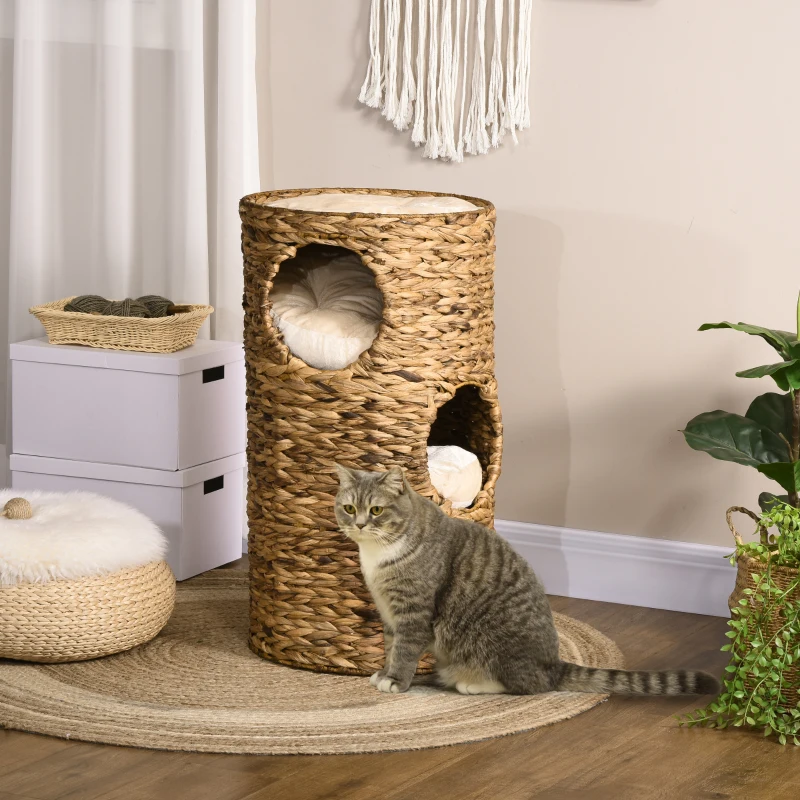 Cat sitting beside a tall woven multi-level cat tower with cushioned hideaway compartments.
