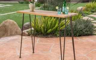 Finished acacia wood bar table with metal legs placed outdoors on patio.