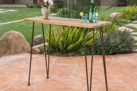 Finished acacia wood bar table with metal legs placed outdoors on patio.