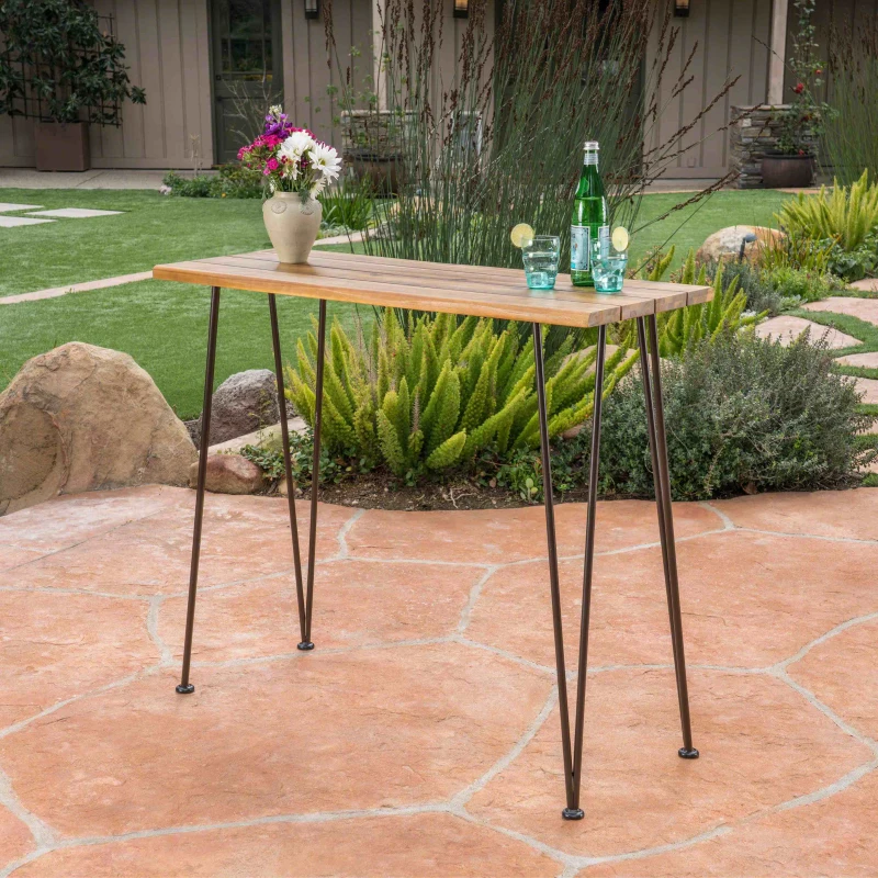 Finished acacia wood bar table with metal legs placed outdoors on patio.