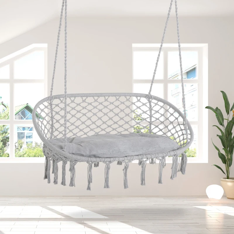 Hanging grey macrame hammock chair with cushion in bright room.
