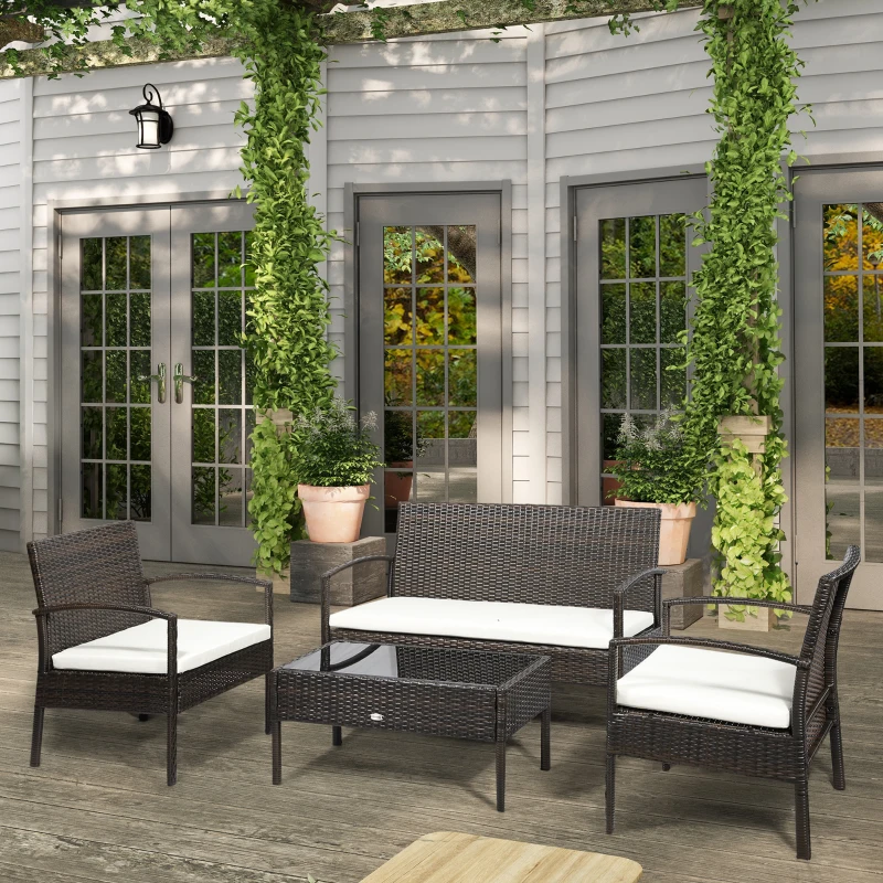 Brown wicker patio conversation set with glass coffee table and white cushions in garden setting.