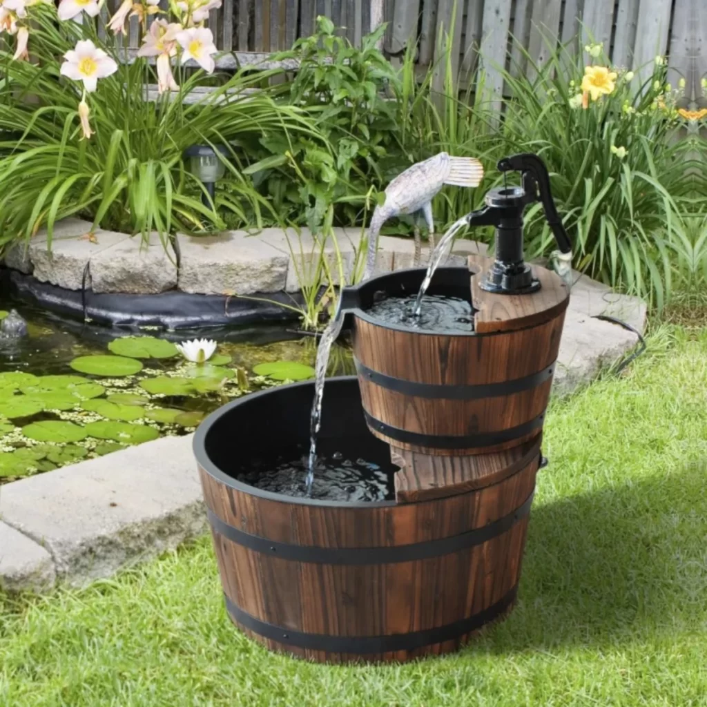 two-tier wooden barrel garden fountain with flowing water displayed beside a backyard pond.
