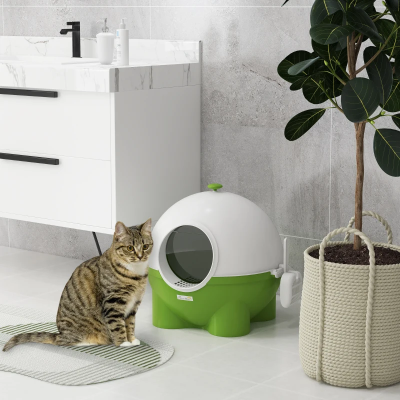Tabby cat sitting beside green and white dome-shaped litter box in modern bathroom.