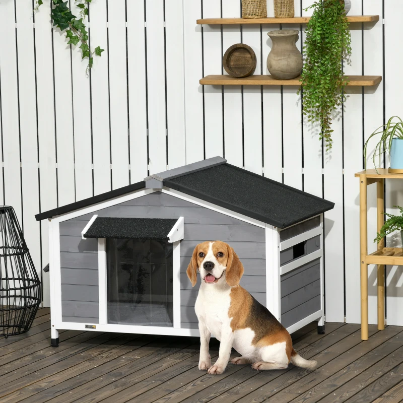 grey wooden outdoor dog house with side window and dog sitting beside the entrance.
