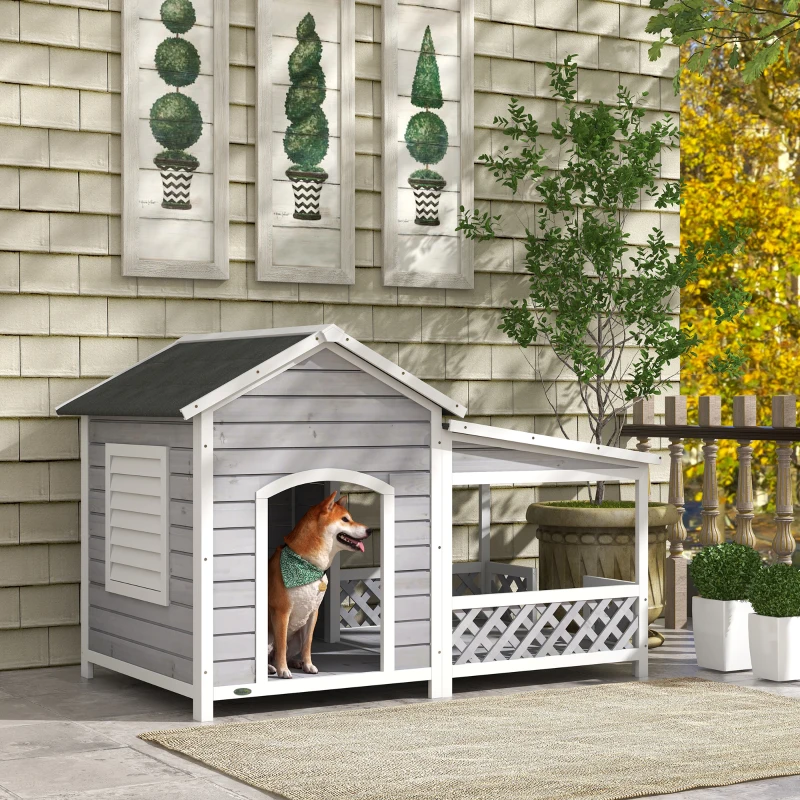 large grey wooden dog house with covered porch and a dog standing at the doorway.